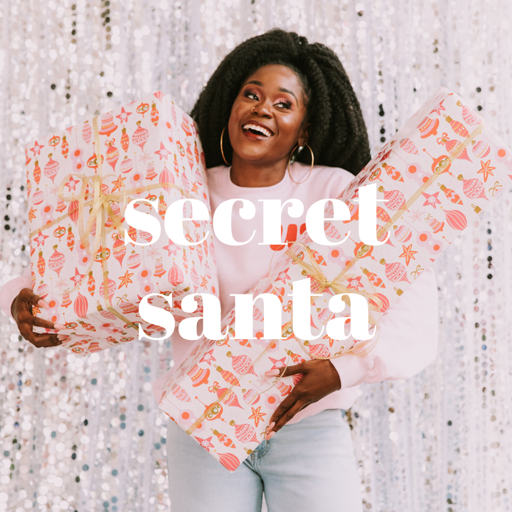 Woman smiling and looking away from the camera holding two large wrapped holiday gifts. She is wearing a Woman-Owned Wallet original sweatshirt.