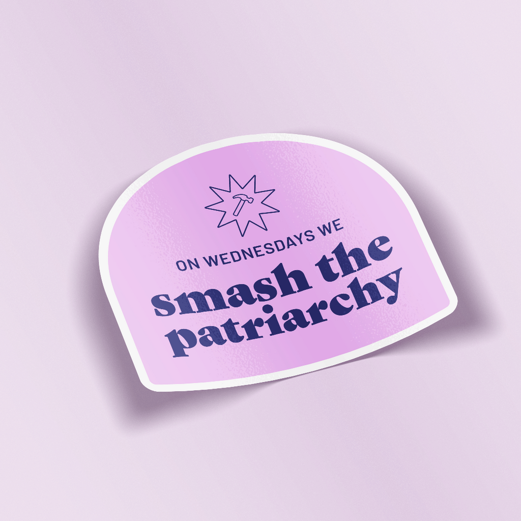 WOW Original decorative sticker that says "On Wednesdays we smash the patriarchy" paired with a hammer symbol all in a deep purple color. The text and illustration is placed on a lilac colored arch. The sticker is laying on a light purple background. 